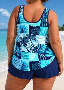 Relaxed tankini set featuring a vibrant blue leaf-print top and navy shorts, worn casually by a model near the water.
