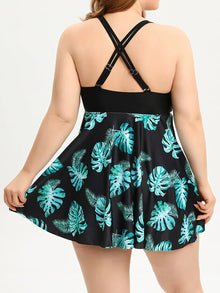Asymmetrical overlay tankini set in black with turquoise tropical print, featuring wide crisscross straps and a flowing silhouette.