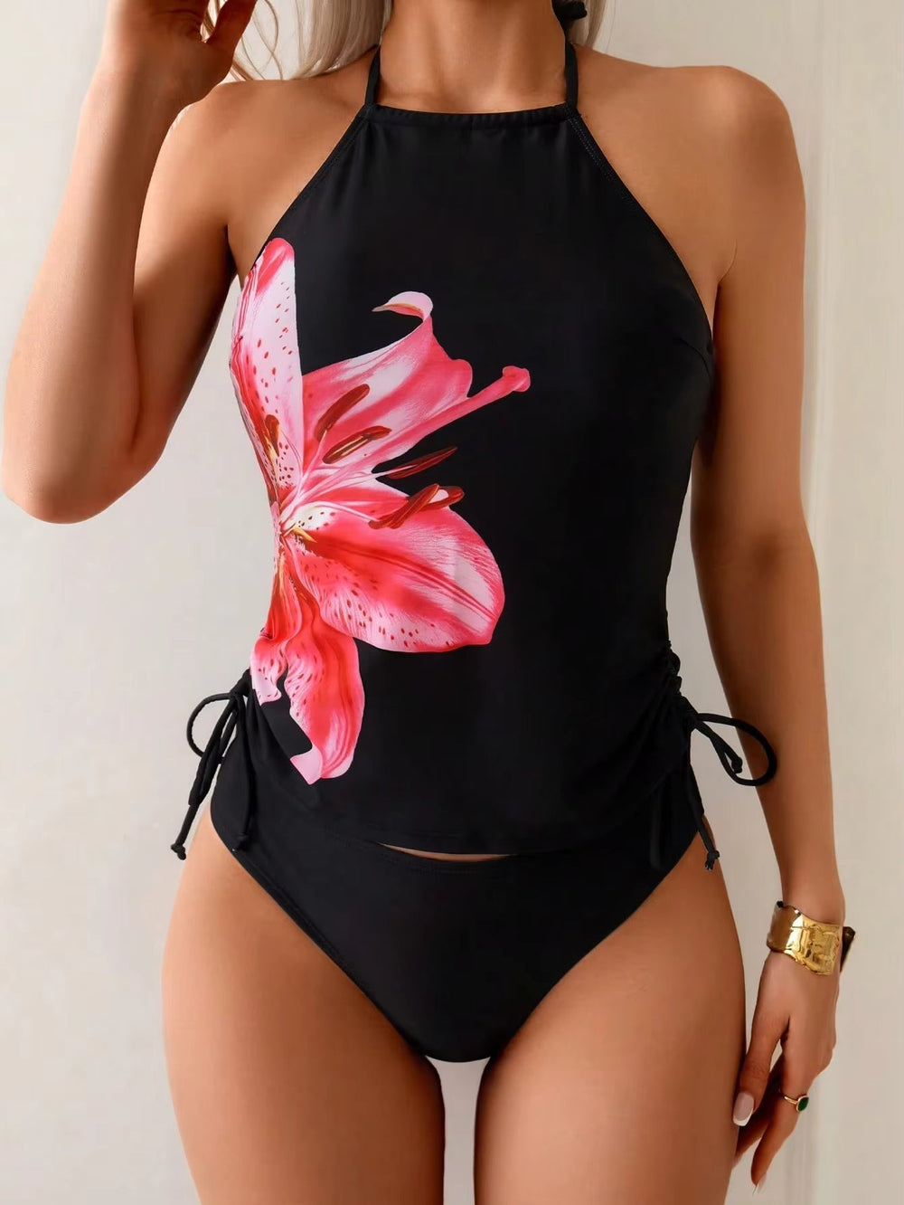 Black tankini set featuring a pink floral print, adjustable side ties, and a squared neckline, styled for summer wear.