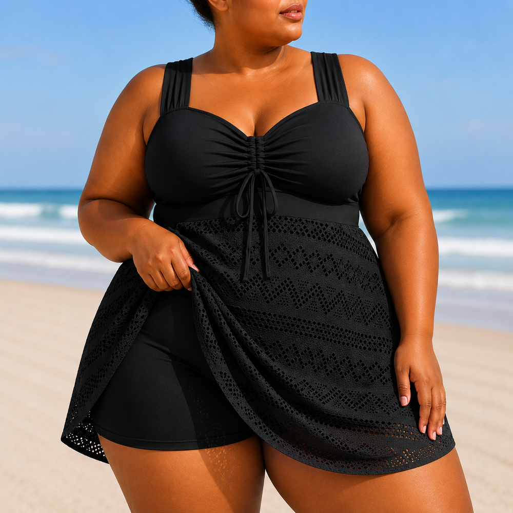 A black one-piece swim dress with a structured top, wide straps, and a flowing skirt overlay featuring a textured pattern.