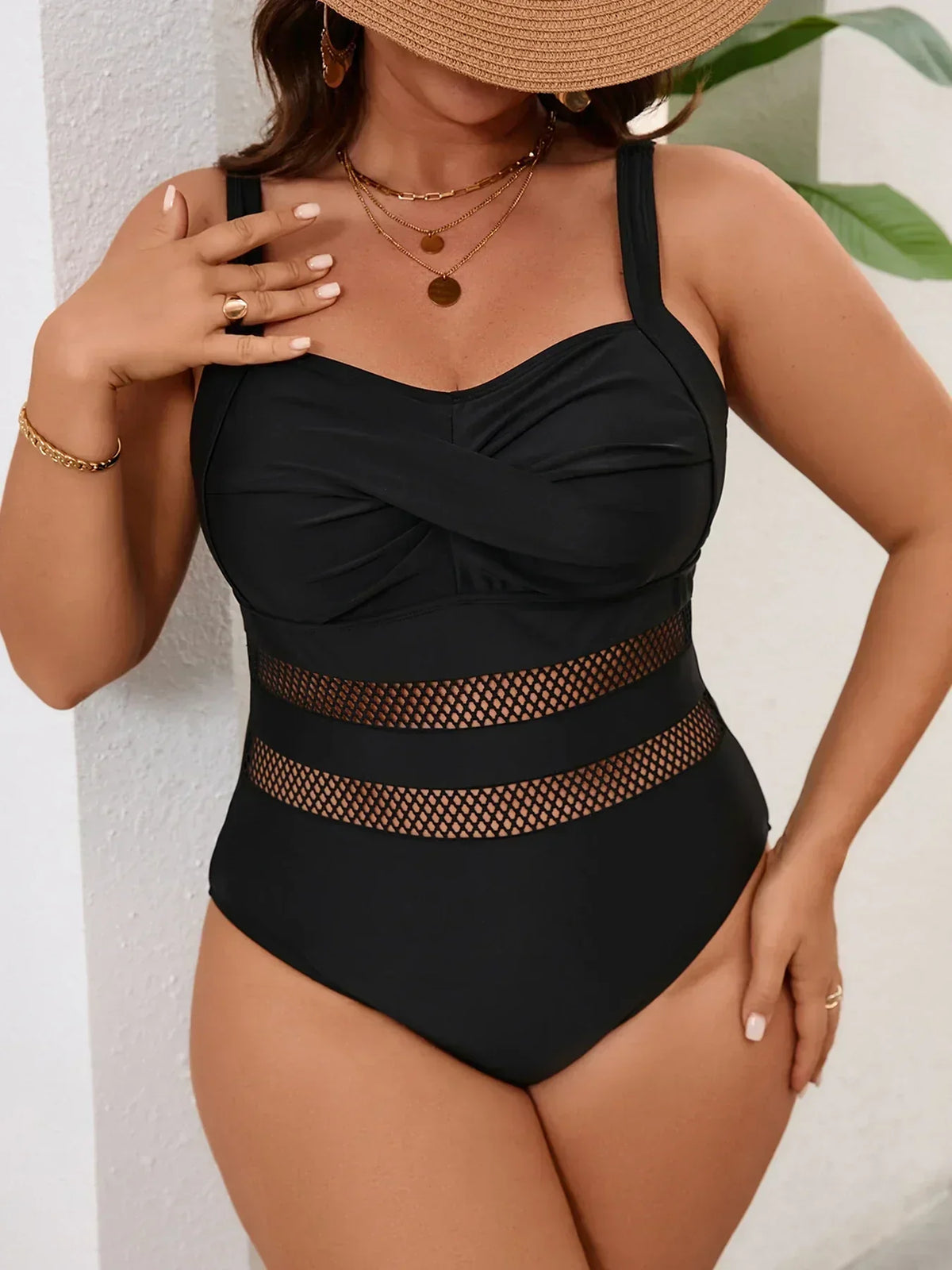 One-piece black swimsuit featuring a V-neckline and sheer paneled detailing, styled with layered gold necklaces.