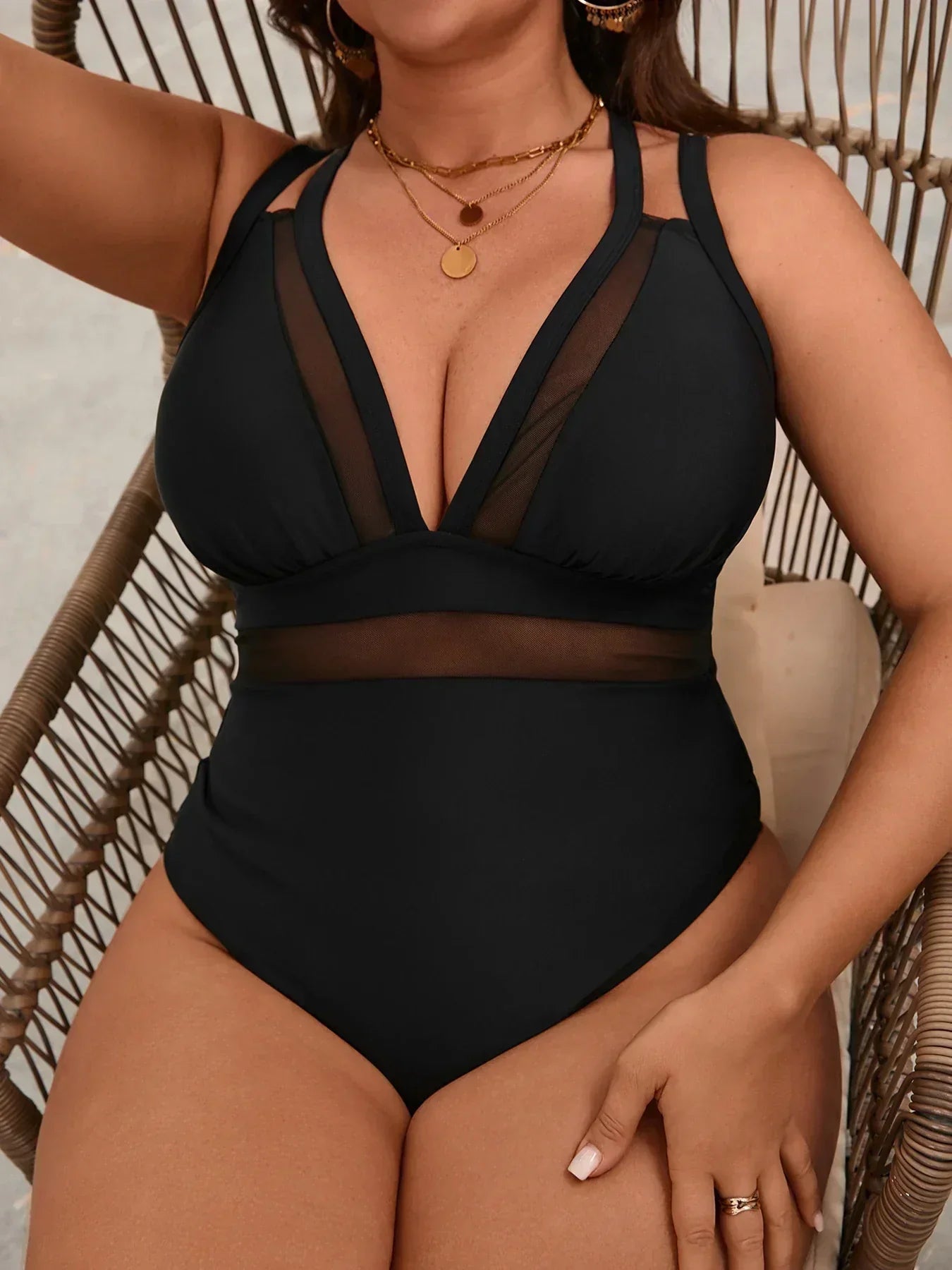 Black one-piece swimsuit with sheer paneled detailing and a flattering V-neckline, styled with layered gold necklaces.
